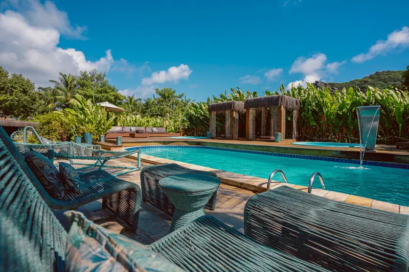 Área da piscina do Dolphin Noronha, com espreguiçadeiras, bangalôs de madeira e jardim.
