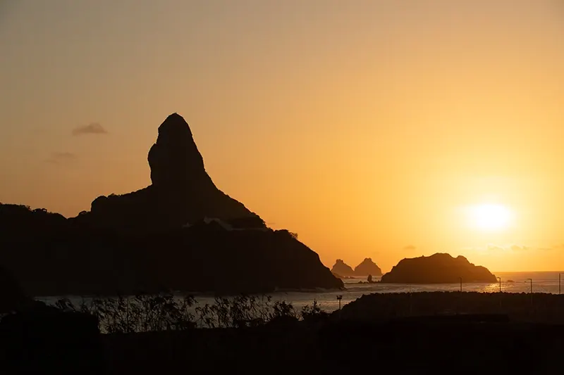 Pôr do sol em Fernando de Noronha, com a silhueta do Morro do Pico contra o céu alaranjado.