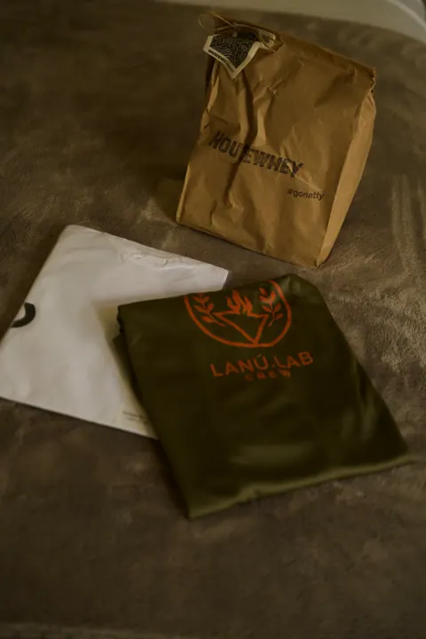 Camiseta verde com a estampa Lanú.Lab Crew ao lado de uma sacola de papel da House Whey, na segunda edição do Lanú.Lab, na Chapada dos Veadeiros, em agosto de 2026.
