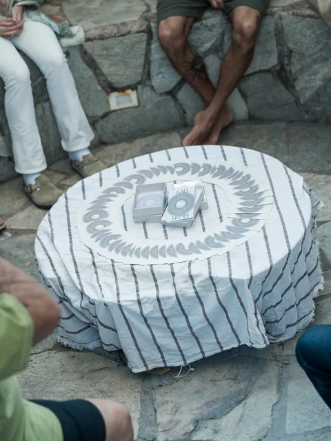 Cartas dispostas em círculo sobre uma mesa redonda coberta por tecido listrado, com pessoas sentadas em volta, na segunda edição do Lanú.Lab, na Chapada dos Veadeiros, em agosto de 2026.