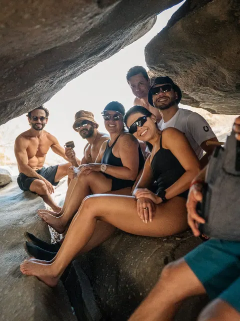 Grupo em trajes de banho sentado em uma fenda entre grandes rochas, sorrindo para a câmera, na segunda edição do Lanú.Lab, na Chapada dos Veadeiros, em agosto de 2026.
